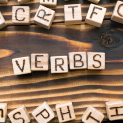 Дерев'яні кубики на столі з літерами, що формують слово "VERBS", символізують вивчення дієслів.