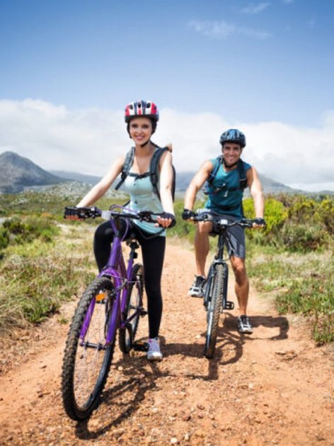 A young couple wearing helmets riding mountain bikes on a sunny trail