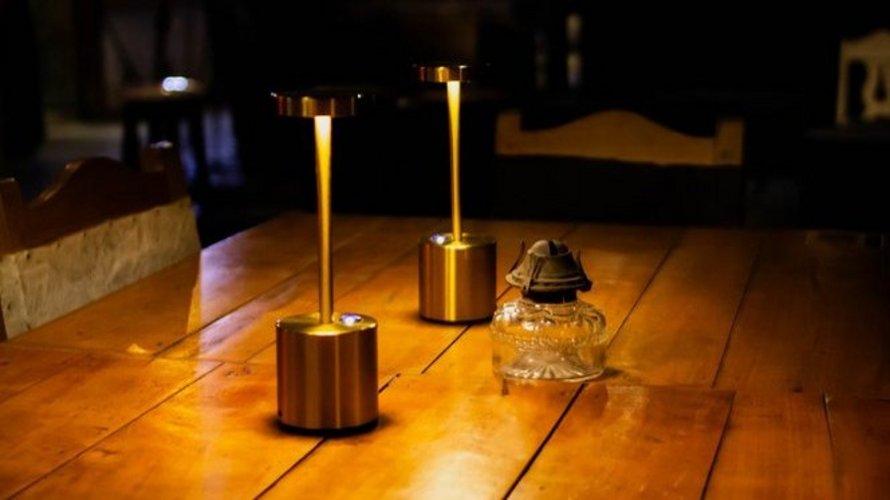 Two modern gold cordless LED table lamps and a vintage glass oil lamp on a wooden table at Fellini restaurant, creating a warm, cozy atmosphere.